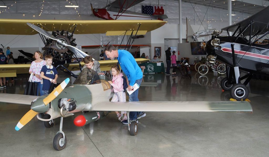 Young girl is shown the cockpit of a small plane while her dad looks also.